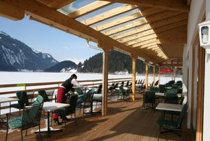 Terrasse mit Tischen und Stühlen, im Hintergrund verschneite Landschaft und See
