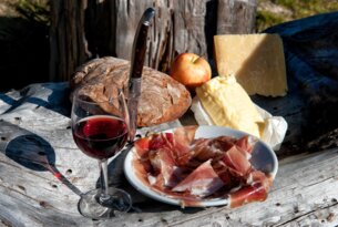 Brot, Käse, Apfel, Schinken und Rotwein auf einem Tisch mit Messer vor einem Holzstapel
