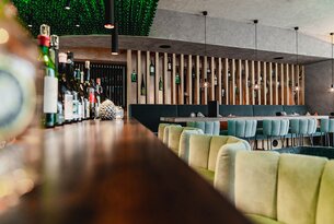 Innenansicht eines Restaurants mit Bar, Flaschen und grünen Sitzbänken