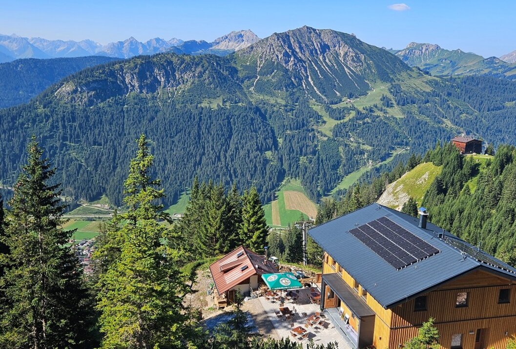 Berghütte mit Solarzellen vor Bergpanorama und bewaldeten Hängen