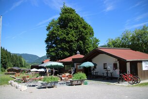 Gasthof mit Biergarten unter Bäumen an einem sonnigen Tag