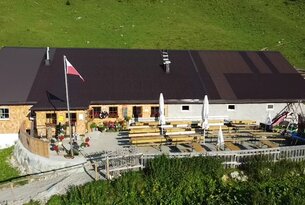 Berghütte mit Terrasse, Tischen, Bänken und polnischer Flagge vor grüner Berglandschaft