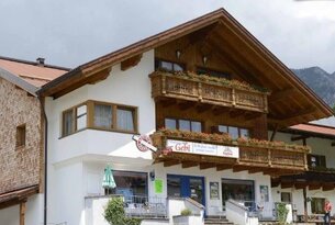 Haus mit Holzbalkonen und Blumenschmuck, darunter ein Geschäft mit blauem Eingang