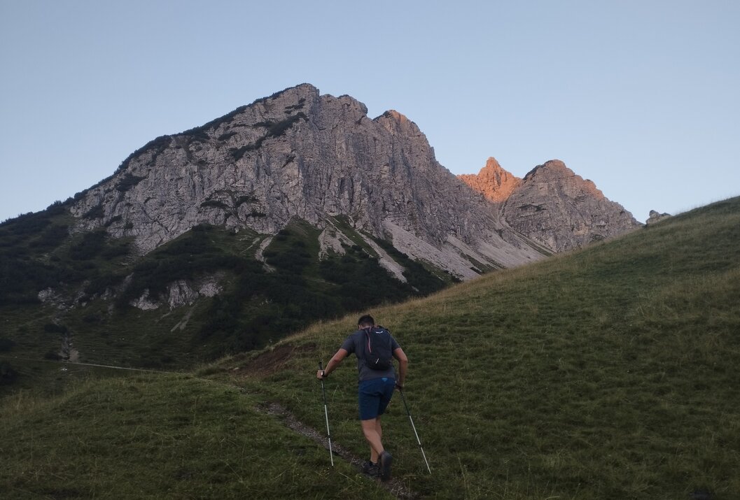 Wanderer mit Stöcken auf Wiese, Berg im Hintergrund