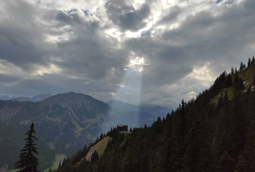 Berghütte auf bewaldetem Hang, Sonnenstrahl durch Wolken