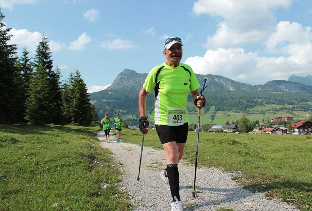 Läufer mit Stöcken auf Schotterweg vor Bergkulisse