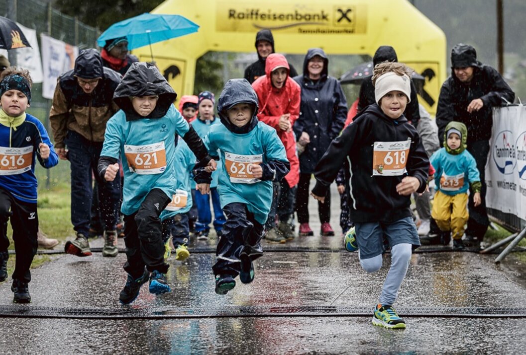 Kinder laufen bei Regen einen Wettlauf, Zuschauer im Hintergrund