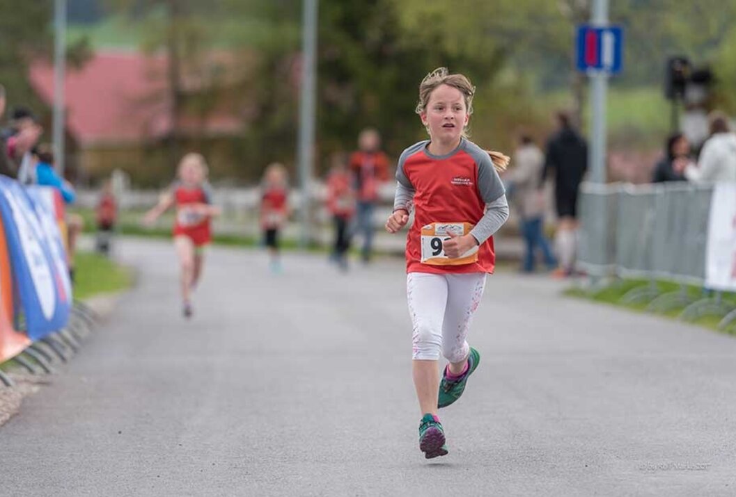 Kind rennt bei einem Lauf mit Startnummer auf einer Straße