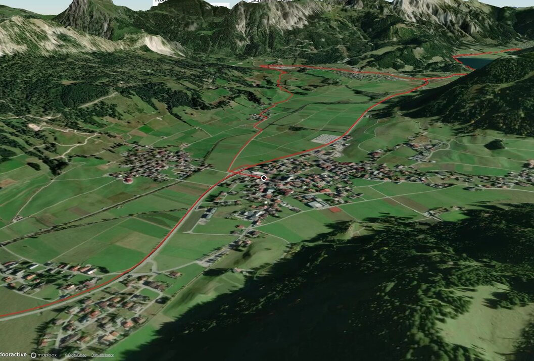 Vogelperspektive auf grüne Landschaft mit Dorf und roter Wegmarkierung