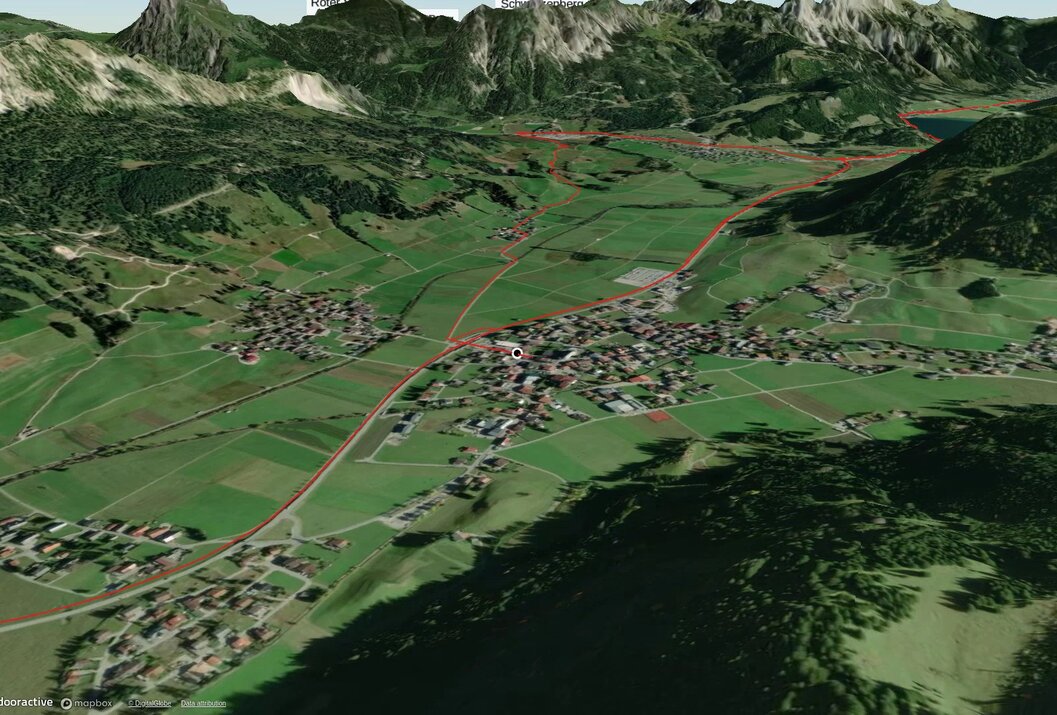 Luftaufnahme einer grünen Landschaft mit Häusern und Bergen im Hintergrund