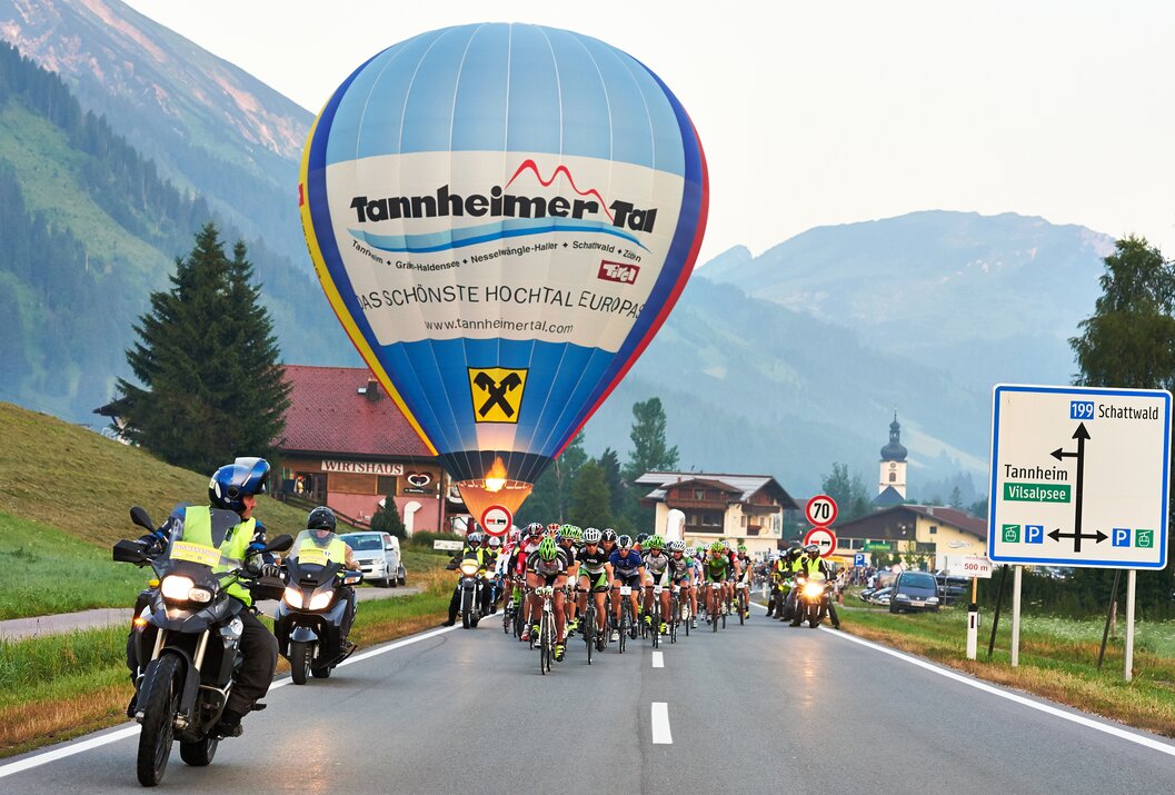 Radrennen auf Straße mit Heißluftballon im Hintergrund