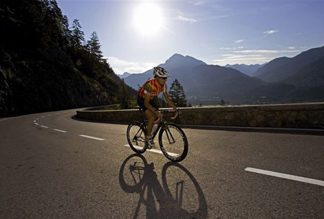 Radfahrer fährt auf Bergstraße, Schatten sichtbar, Berge im Hintergrund