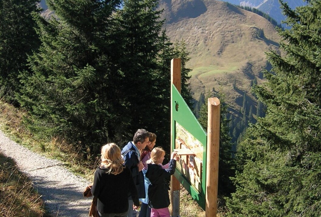 Familie an Infotafel auf Wanderweg in den Bergen