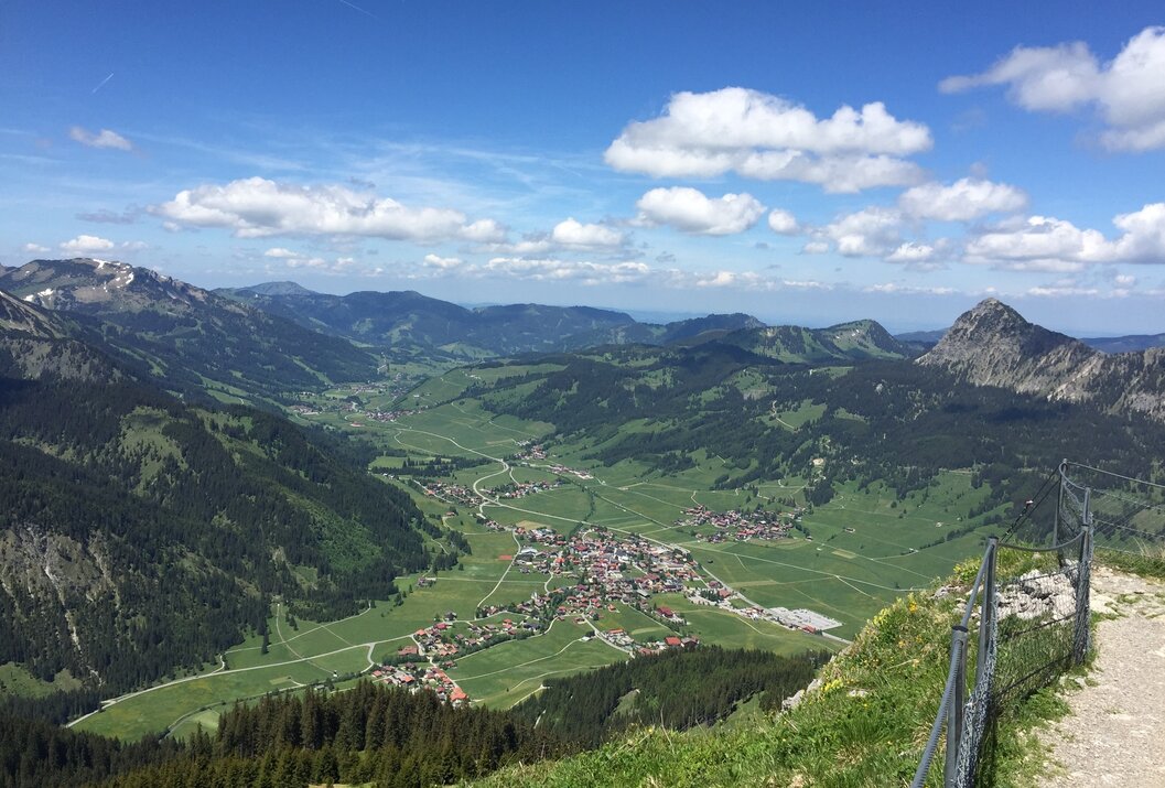Weite grüne Landschaft mit Bergen und einem Dorf unter blauem Himmel