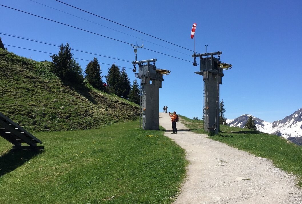 Berglandschaft mit Weg, Liftstützen und schneebedeckten Gipfeln unter blauem Himmel