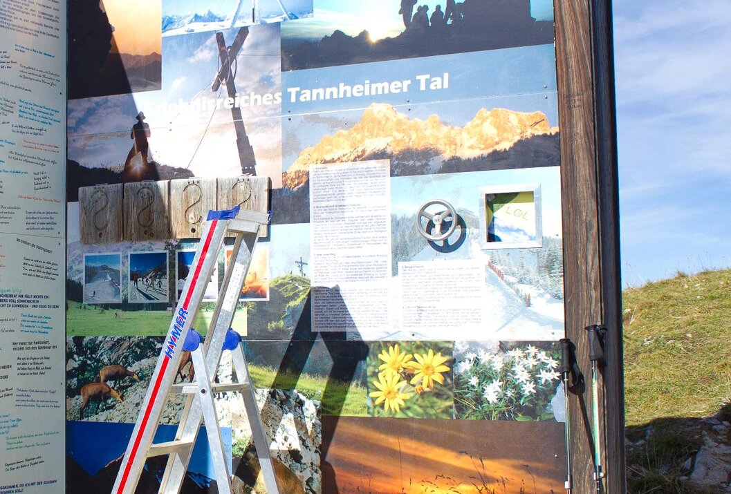 Informationstafel mit Bergmotiven und Leiter davor