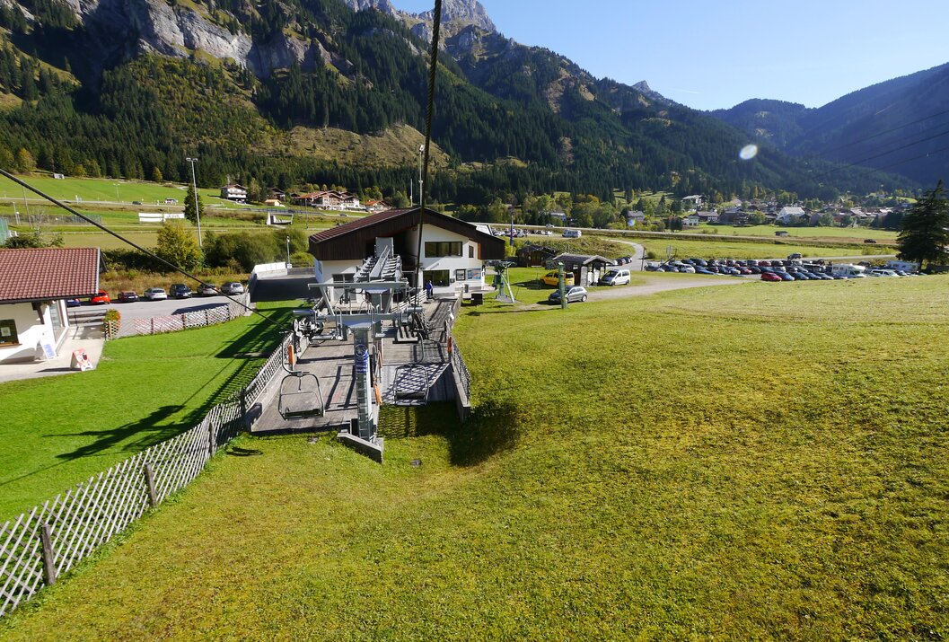 Blick von Seilbahn auf Talstation, grüne Wiese, Gebäude und Berglandschaft