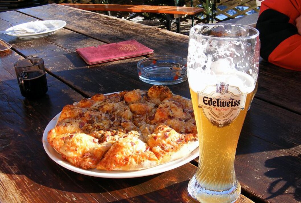 Pizza, Bierglas Edelweiss, Aschenbecher und rotes Buch auf Holztisch
