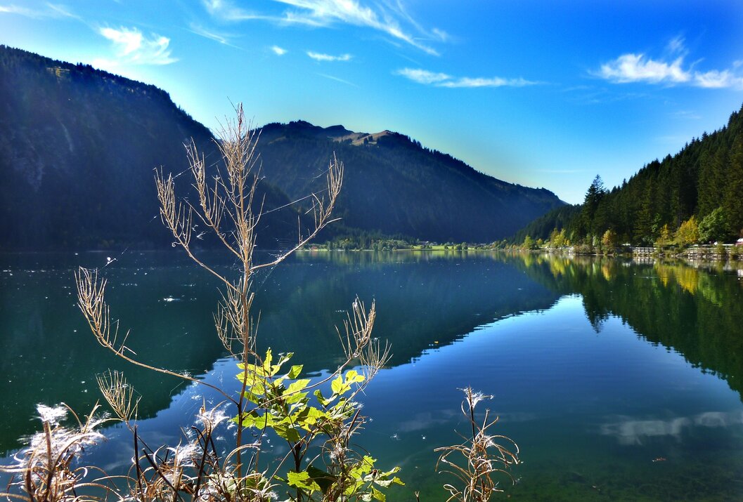 Bergsee mit Spiegelung, bewaldeten Bergen und blauem Himmel