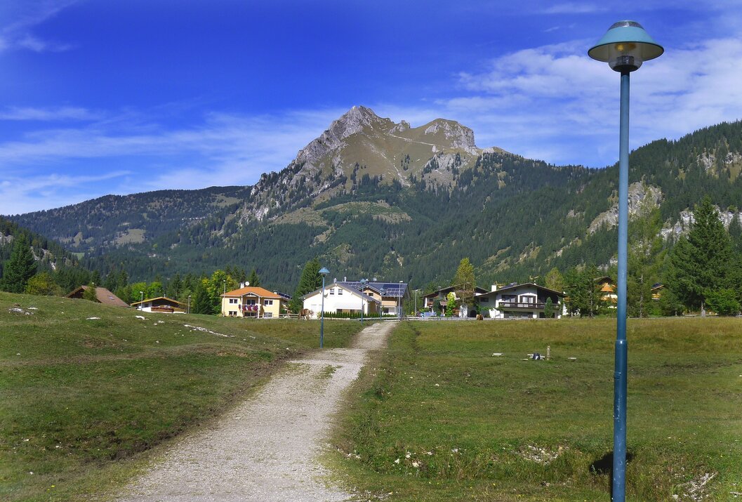 Berglandschaft mit Häusern, Weg und Straßenlaterne unter blauem Himmel