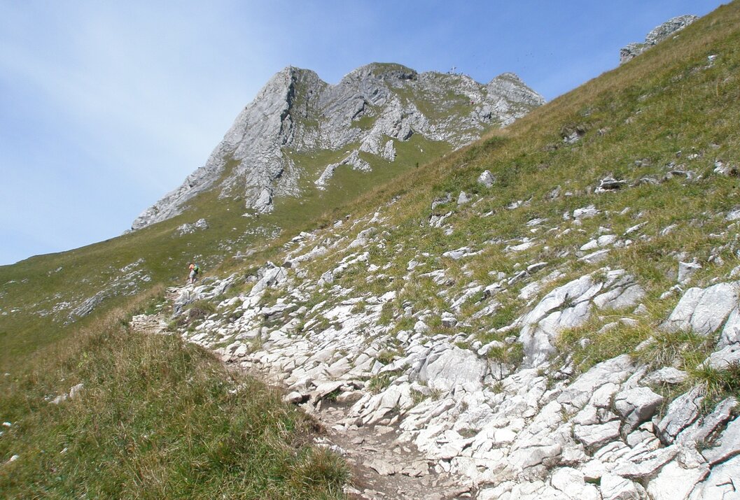 Bergpfad führt steil bergauf zu einem felsigen Gipfel unter blauem Himmel