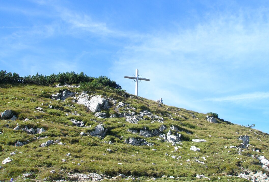 Gipfelkreuz auf grünem Hügel unter blauem Himmel