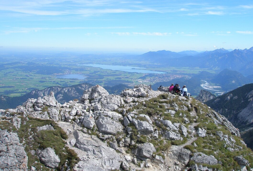 Berggipfel mit Menschengruppe, Blick auf Seen und grüne Landschaft unter blauem Himmel