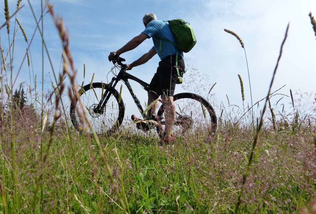 Mann fährt Mountainbike durch hohes Gras unter blauem Himmel