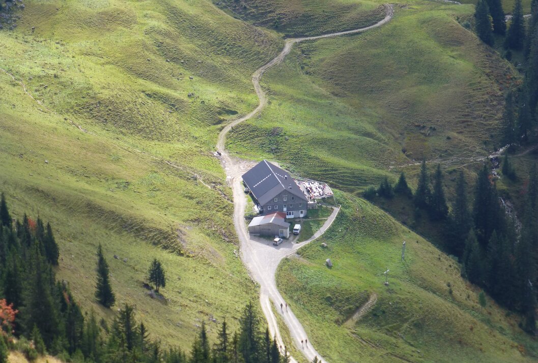 Berghütte auf grüner Wiese, gewundener Pfad führt hinauf