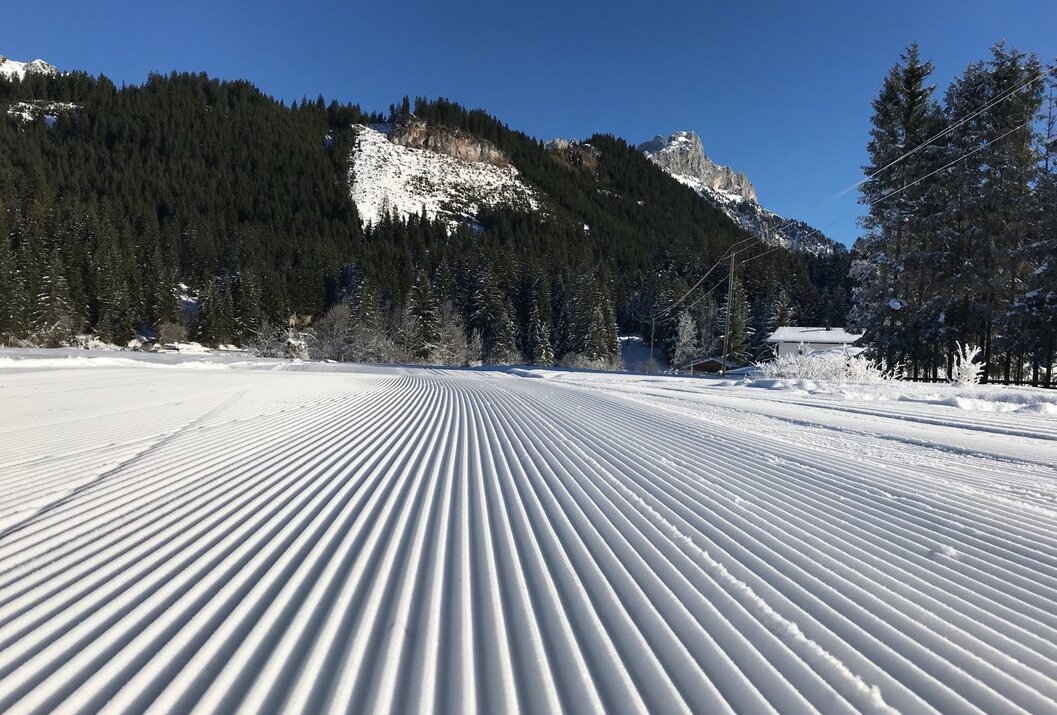 Frisch präparierte Skipiste vor bewaldetem Berg an sonnigem Tag