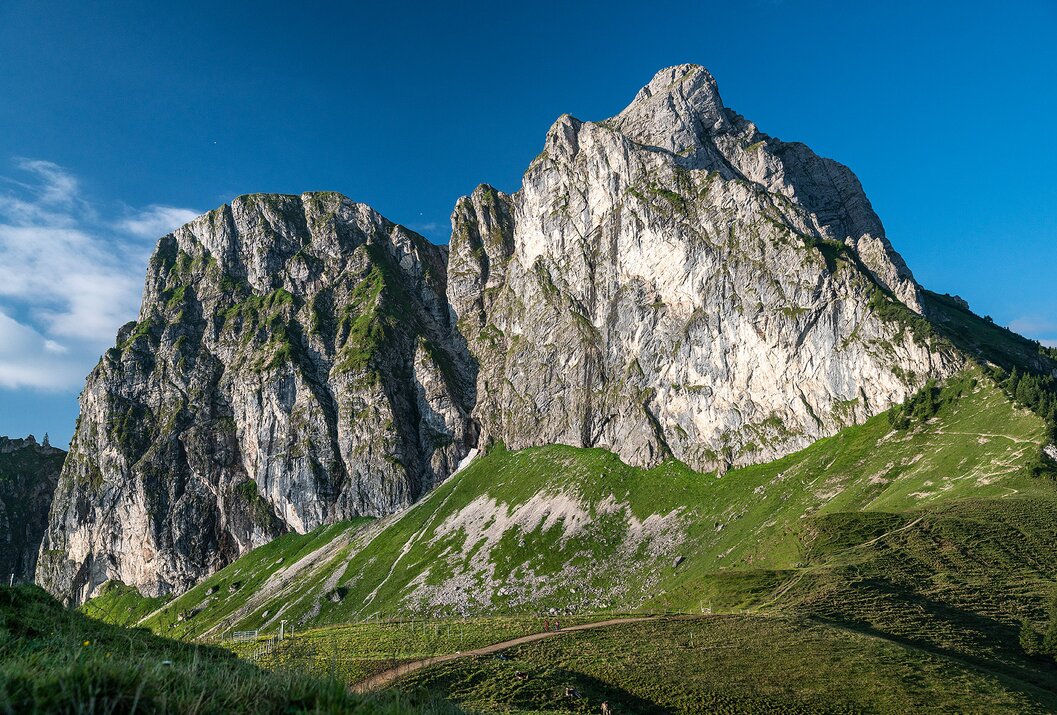 Berglandschaft mit steilen Felswänden und grünen Wiesen unter blauem Himmel