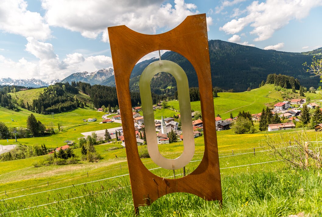 Skulptur mit ovalem Glaseinsatz vor Berglandschaft