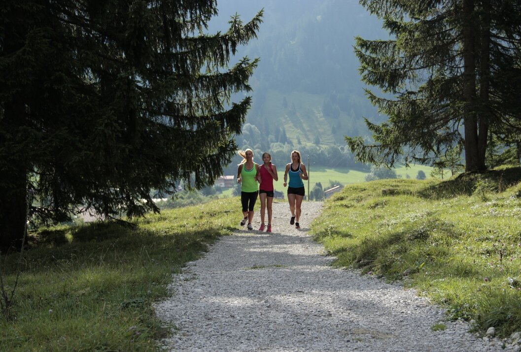 Drei Frauen joggen auf einem Schotterweg vor einer Bergkulisse