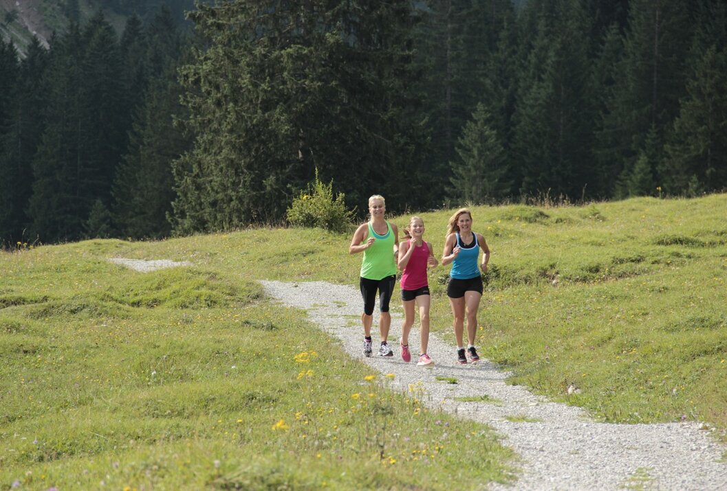 Drei Frauen joggen auf einem Pfad durch eine grüne Landschaft mit Bäumen im Hintergrund