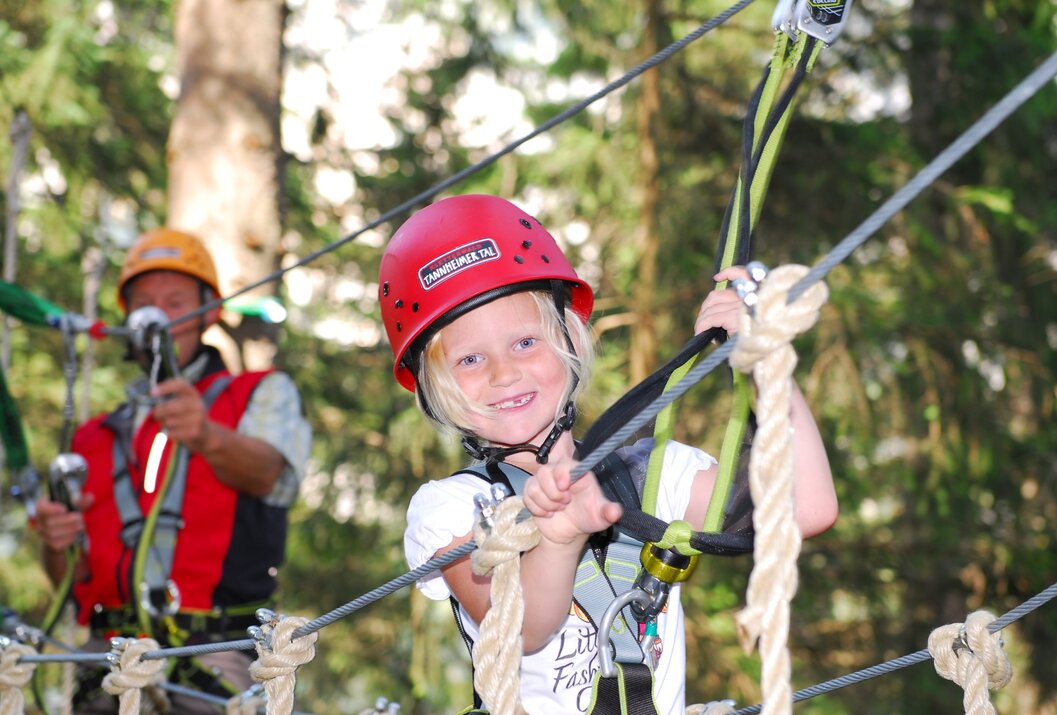 Mädchen mit rotem Helm im Hochseilgarten lächelt in die Kamera