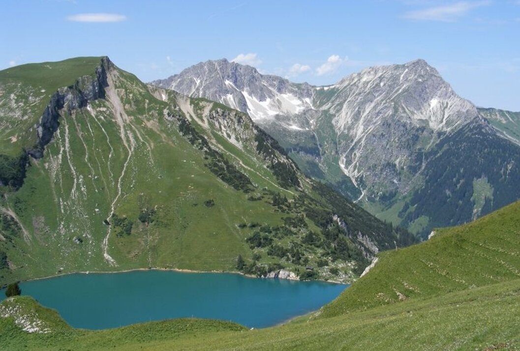 Berglandschaft mit grünem Hang und blauem See im Vordergrund