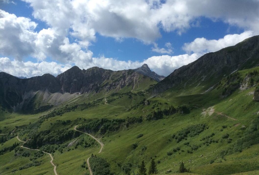 Grüne Berglandschaft mit gewundenen Pfaden unter blauem Himmel mit Wolken