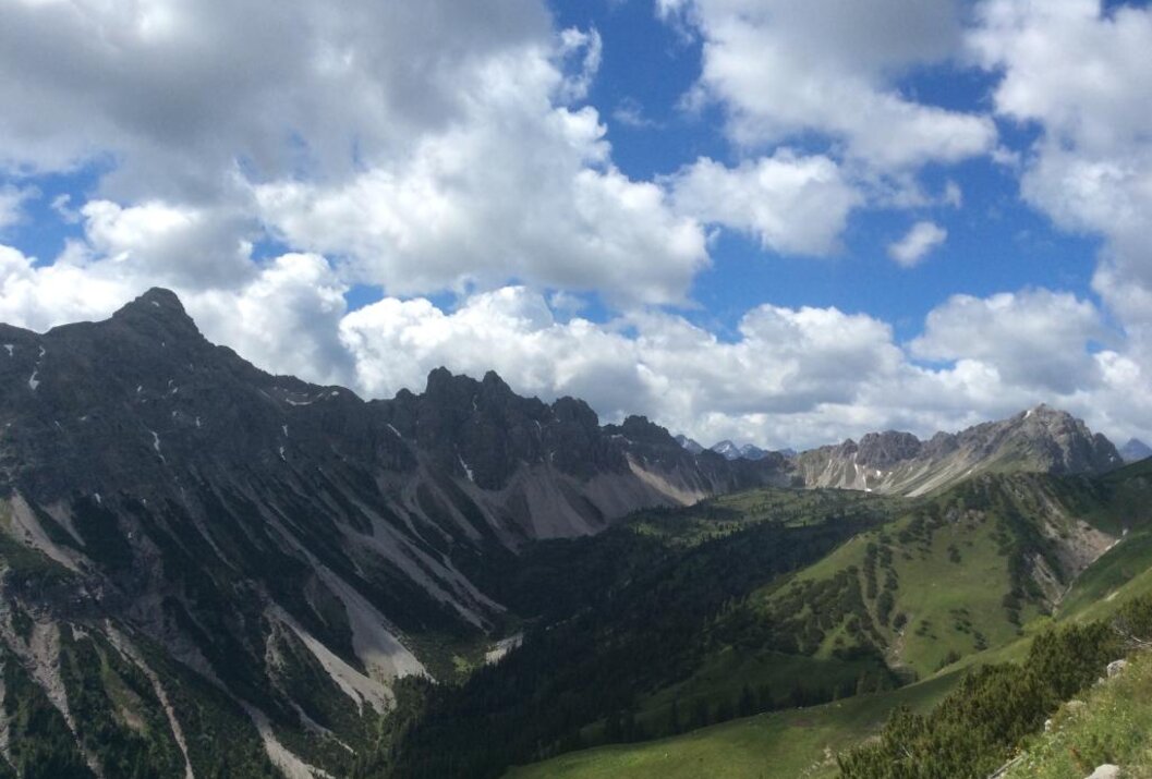 Berglandschaft mit grünen Wiesen und felsigen Gipfeln unter blauem Himmel mit Wolken