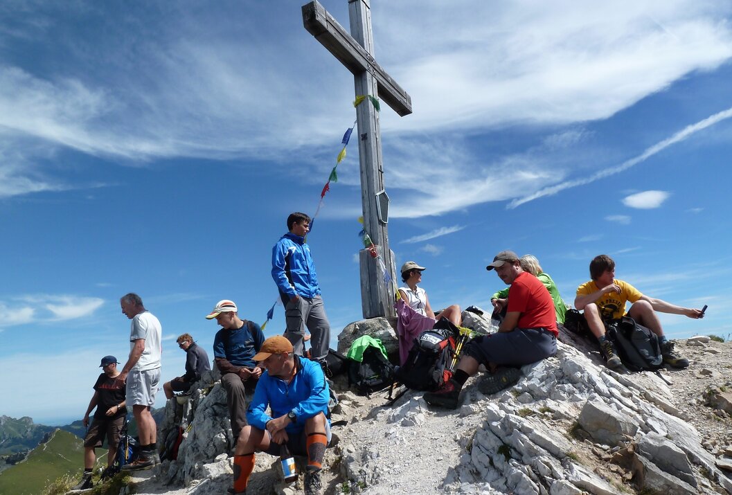Menschengruppe rastet am Gipfelkreuz auf einem Berg