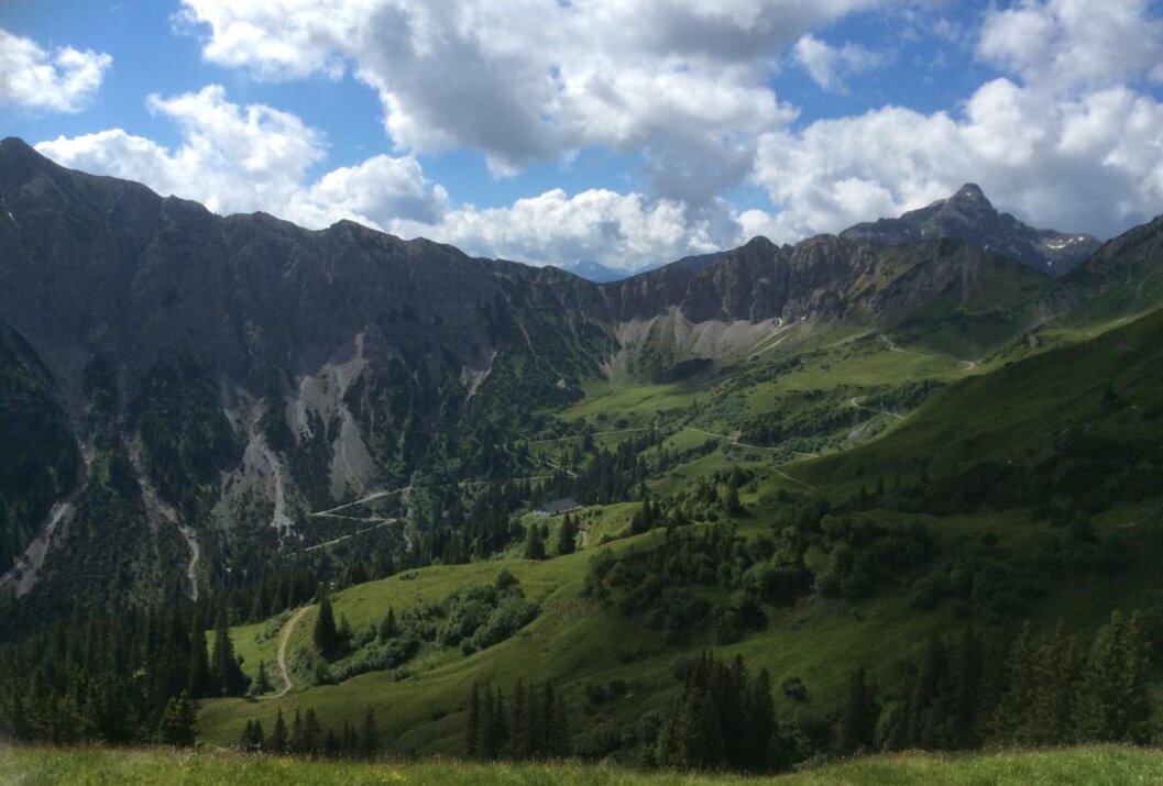Grüne Berglandschaft mit bewaldeten Hängen unter blauem Himmel mit Wolken