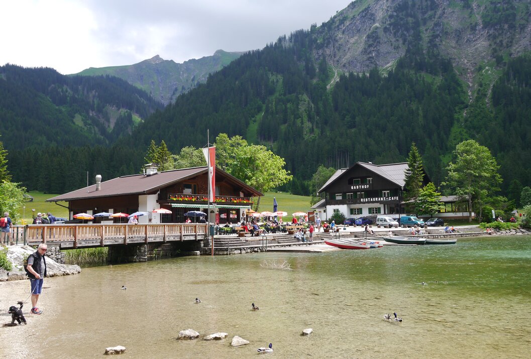 See mit Gebäuden, Brücke, Menschen und Bergen im Hintergrund