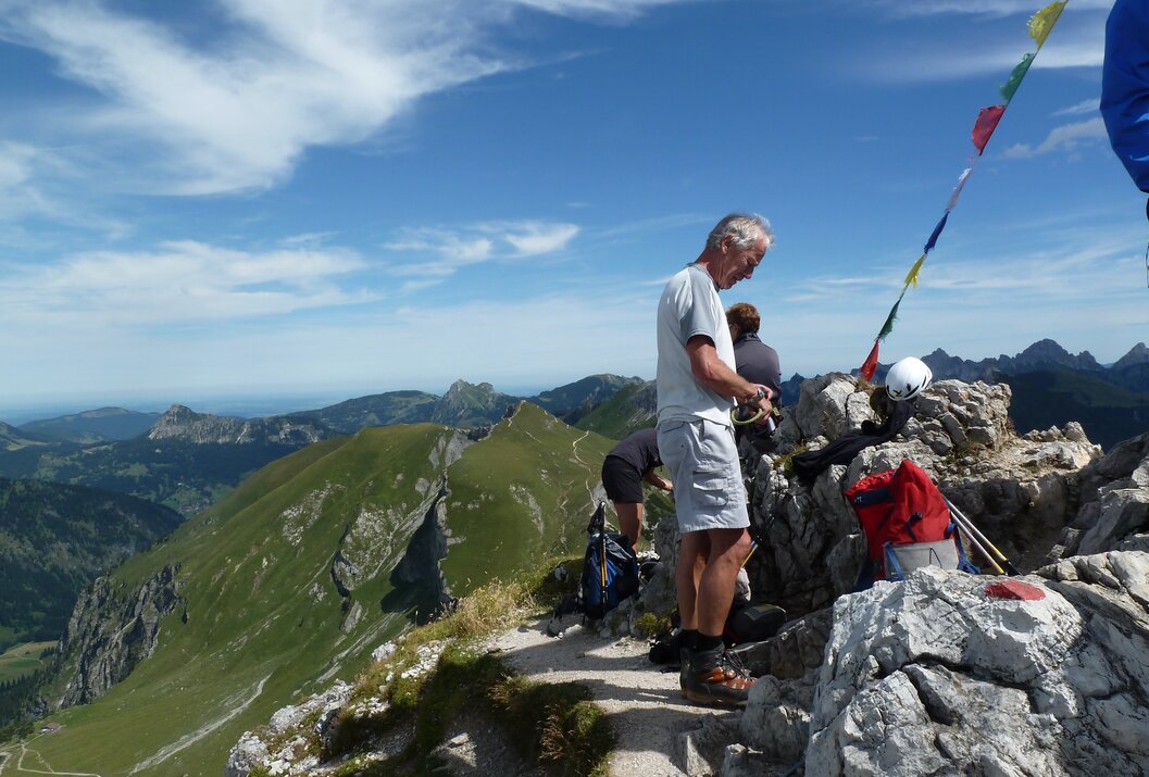 Wanderer steht auf Berggipfel, blickt nach unten, grüne Landschaft im Hintergrund
