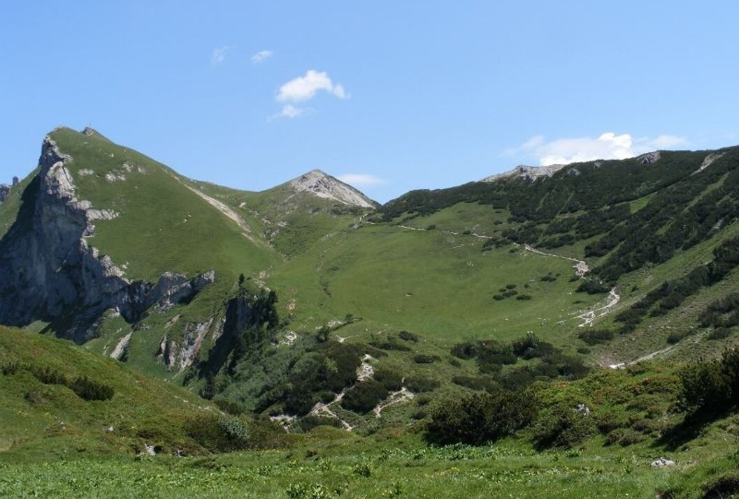 Grüne Berglandschaft unter blauem Himmel mit einzelnen Wolken