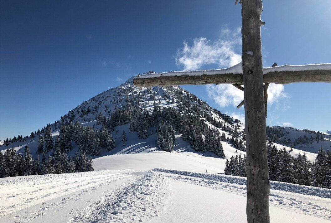 Verschneiter Berg unter blauem Himmel mit Holzkreuz im Vordergrund