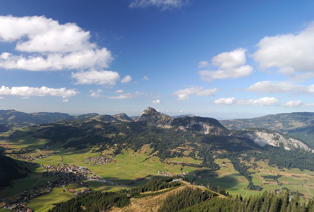 Berglandschaft mit grünen Wiesen, Wäldern und blauem Himmel mit Wolken