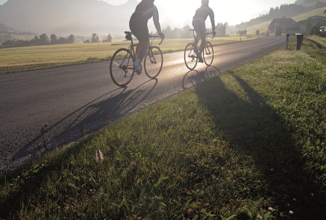 Zwei Radfahrer fahren auf einer Straße in Richtung Sonne