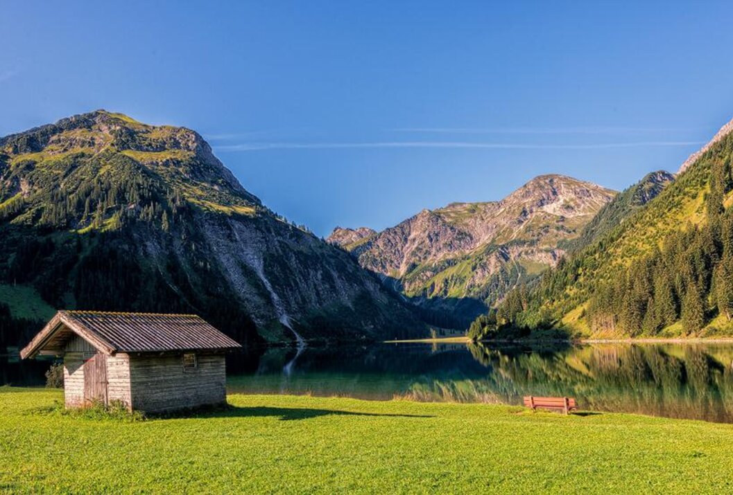 Hütte am Seeufer vor Bergpanorama unter blauem Himmel