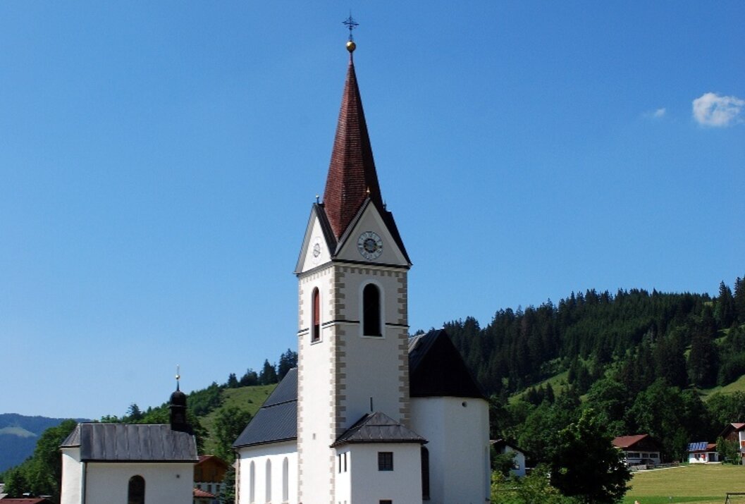 Weiße Kirche mit rotem Kirchturm vor blauem Himmel und grüner Landschaft