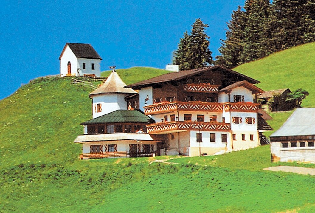 Hotelgebäude auf grünem Hügel, kleine Kapelle im Hintergrund