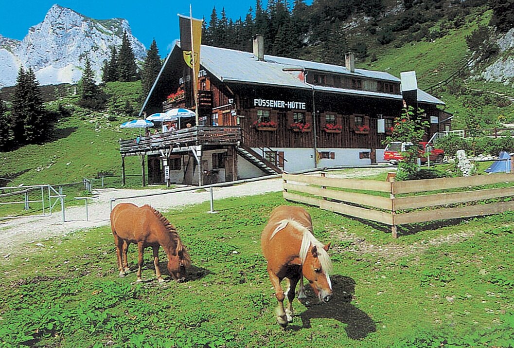 Füssener Hütte mit zwei Pferden auf einer Wiese vor dem Gebäude